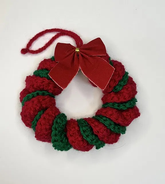 Ghirlanda di Natale a uncinetto, realizzata in rosso e verde e decorata con un fiocco rosso di stoffa. Il modello è di Keely Robertson.